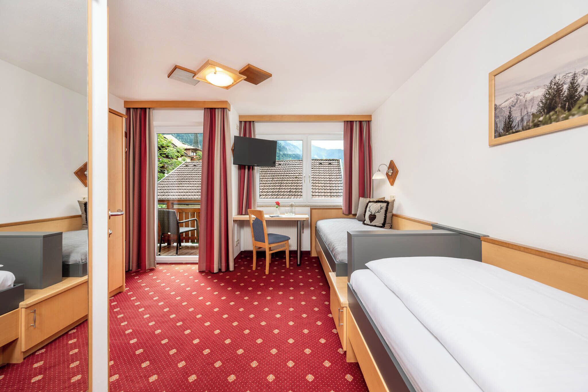 A hotel room with a bed, a desk, a chair, a television, and a window with a view of mountains.