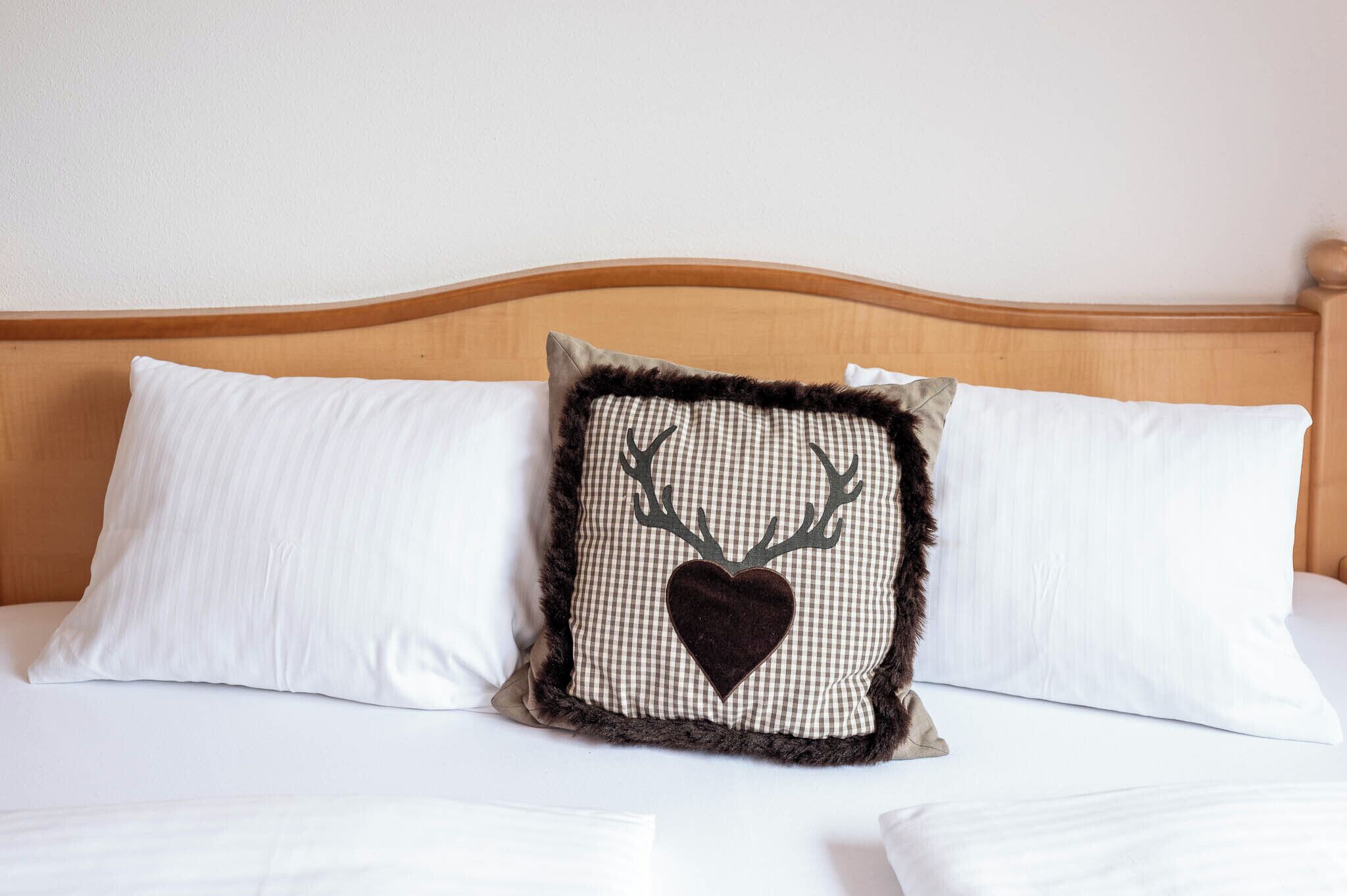 A bed with two white pillows and a decorative pillow with a deer head and heart design.