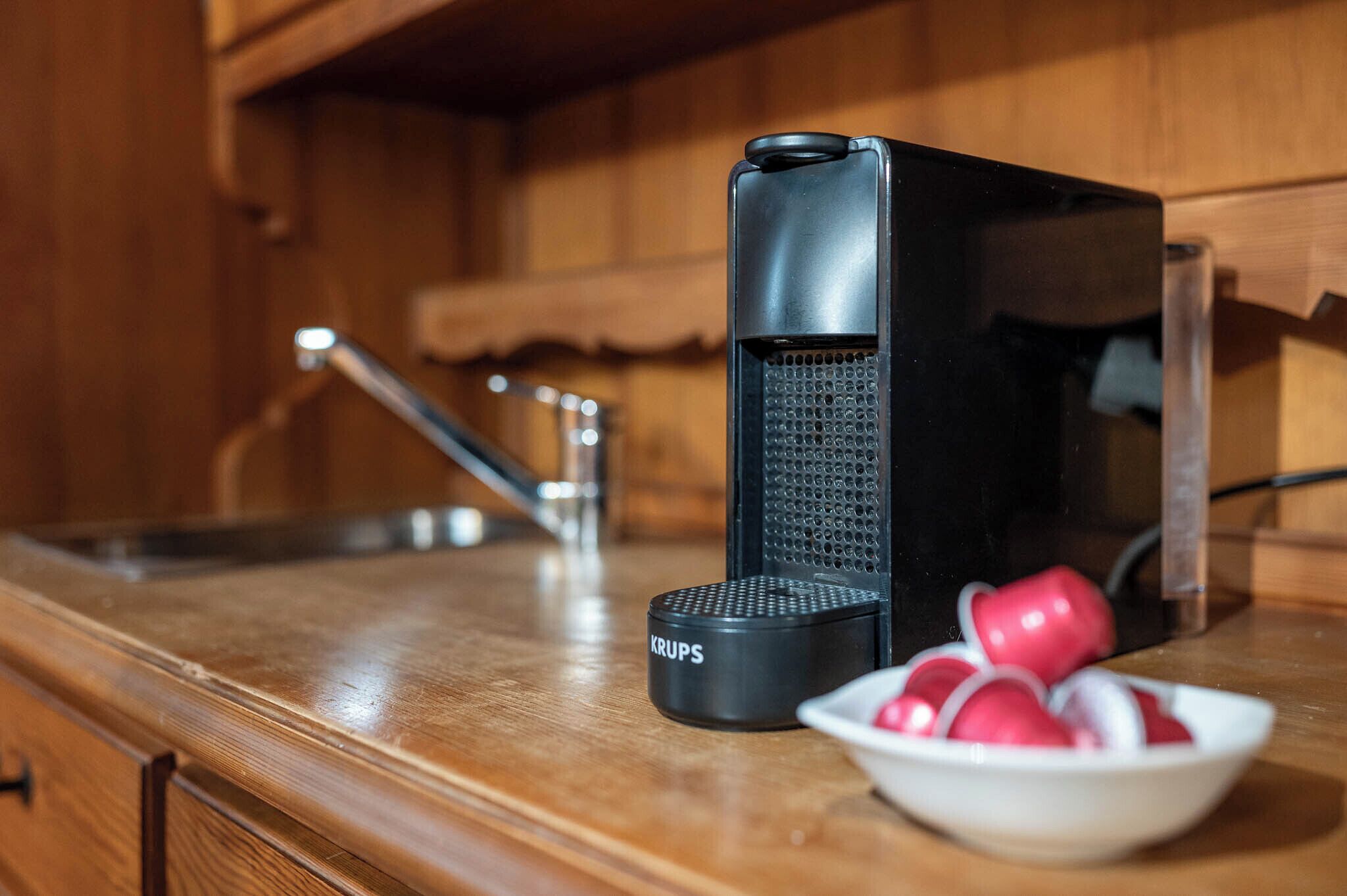 Una cocina con cafetera, un frutero y un lavamanos.