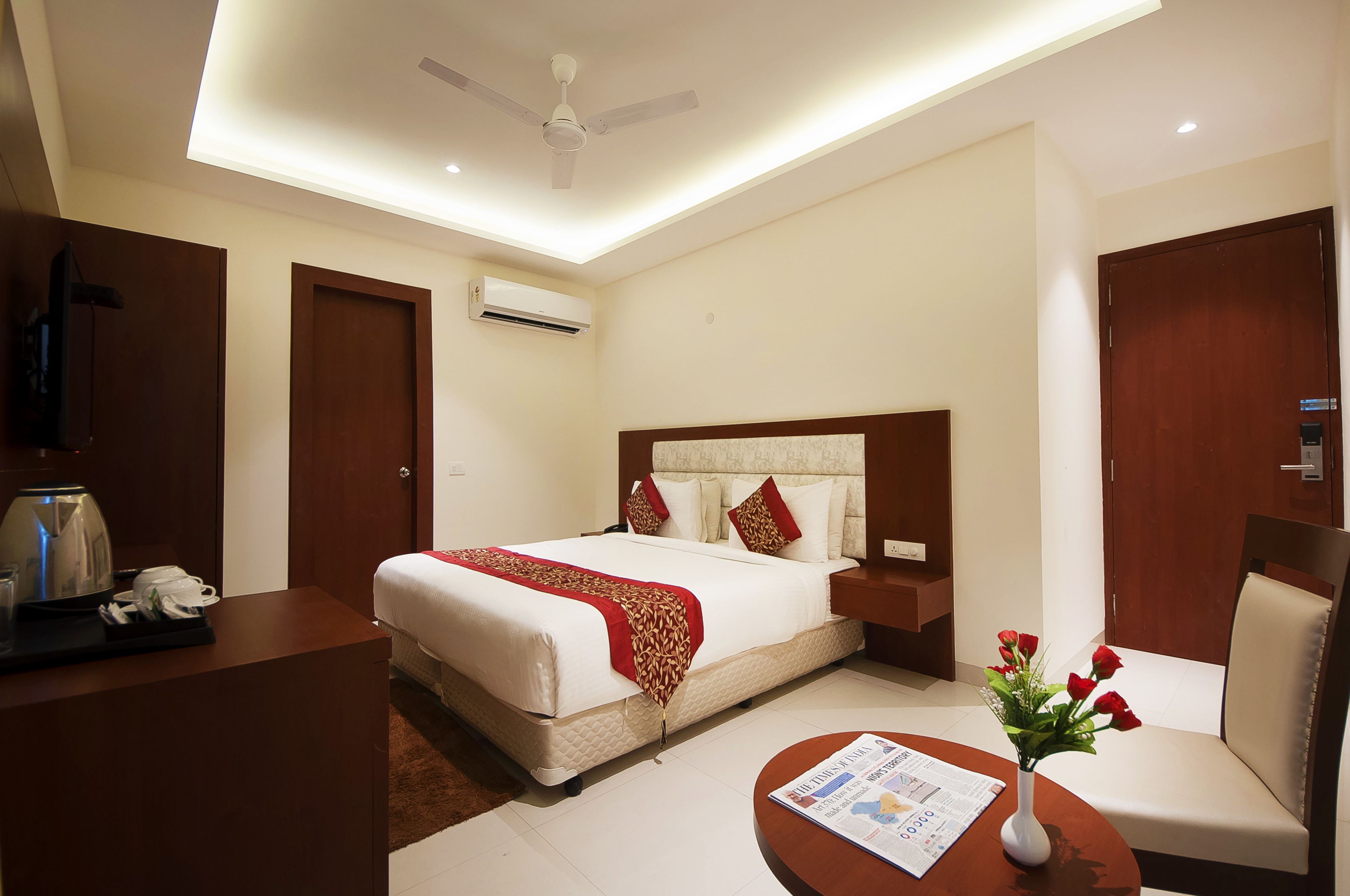 A hotel room with a bed, a desk, a chair, a vase with flowers, and a ceiling fan.