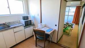 Une cuisine compacte équipée d’un four à micro-ondes, d’un grille-pain et d’un évier. On y trouve une petite table avec une chaise, ainsi qu’une porte coulissante donnant sur un balcon avec vue.