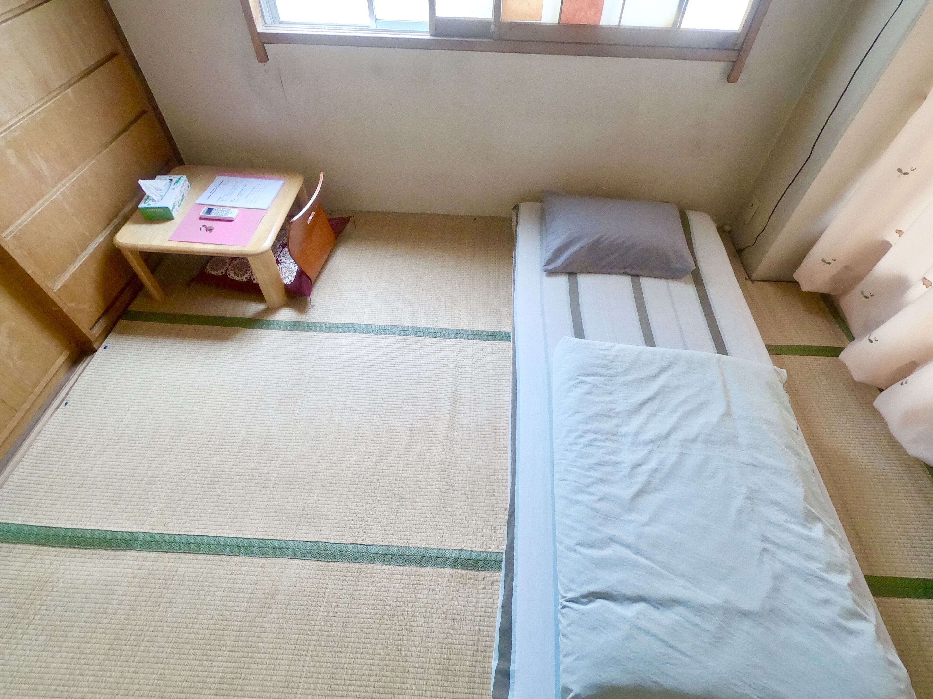 A small, neatly arranged room with a bed, a small table, and a window.