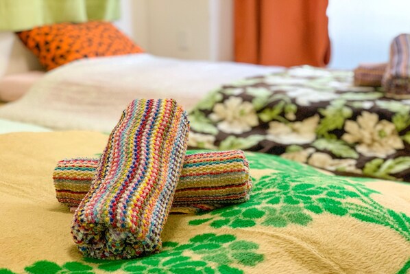 A bed with a green and beige blanket, a colorful striped blanket, and a floral patterned pillow.