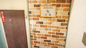 Un mur de briques sur lequel est fixée une plaque encadrée portant l’inscription « TOKYOACCOMMO » et des caractères chinois.