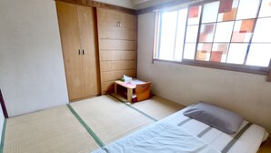 Une pièce avec un sol recouvert de tatamis, un lit avec un oreiller, une petite table en bois avec une boîte de mouchoirs et une armoire.