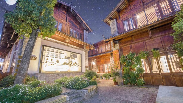 A courtyard with wooden buildings, a large illuminated mural, and potted plants. - Li Jiang Tang Feng Yard No.1 (Lijiang)