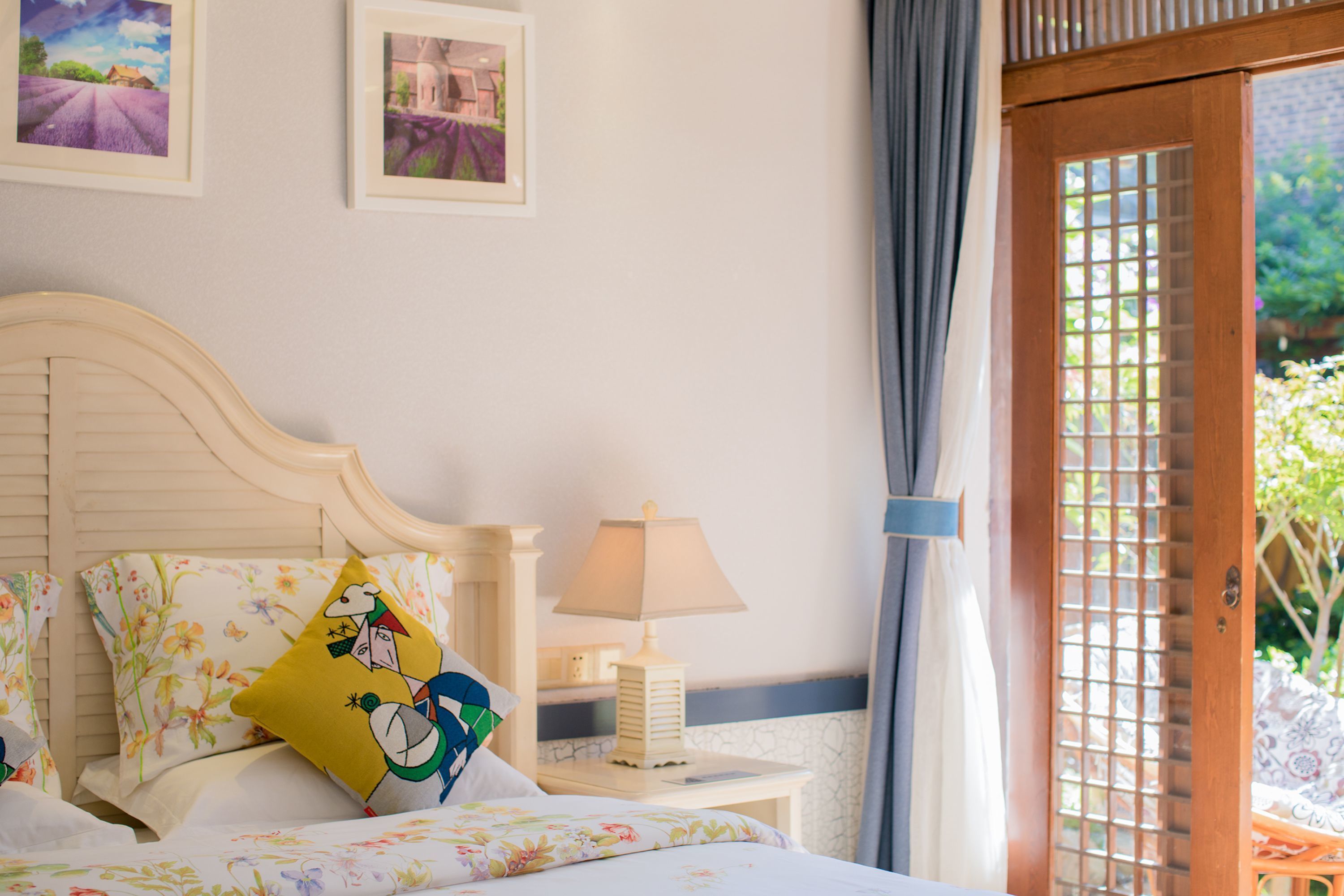A bedroom with a bed, pillows, a bedside table with a lamp, and a view through a wooden door.