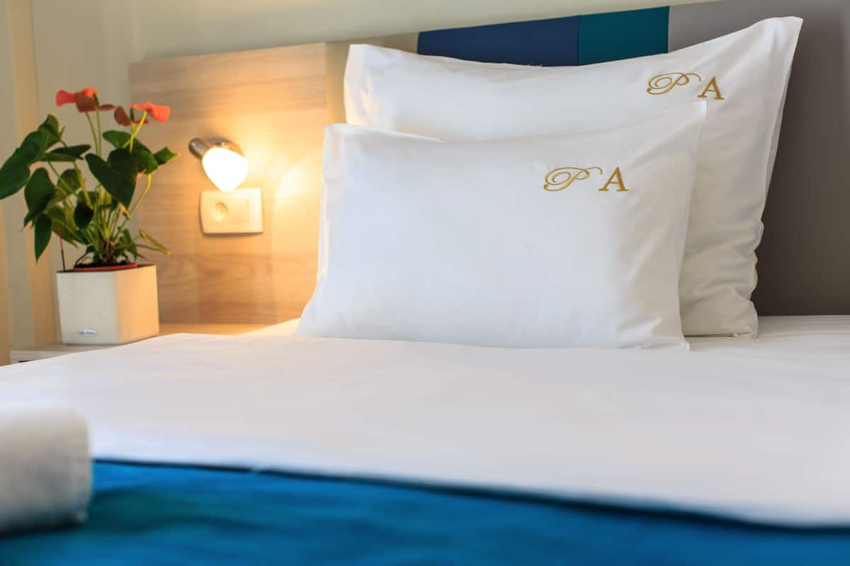Un lit bien fait, avec du linge de lit blanc et des oreillers ornés de motifs brodés représentant des initiales.