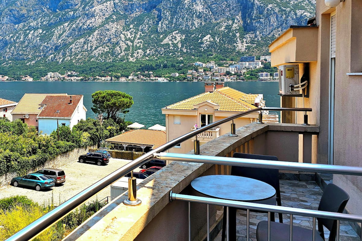Un balcon avec une table et des chaises, donnant sur un lac avec des montagnes en arrière-plan.