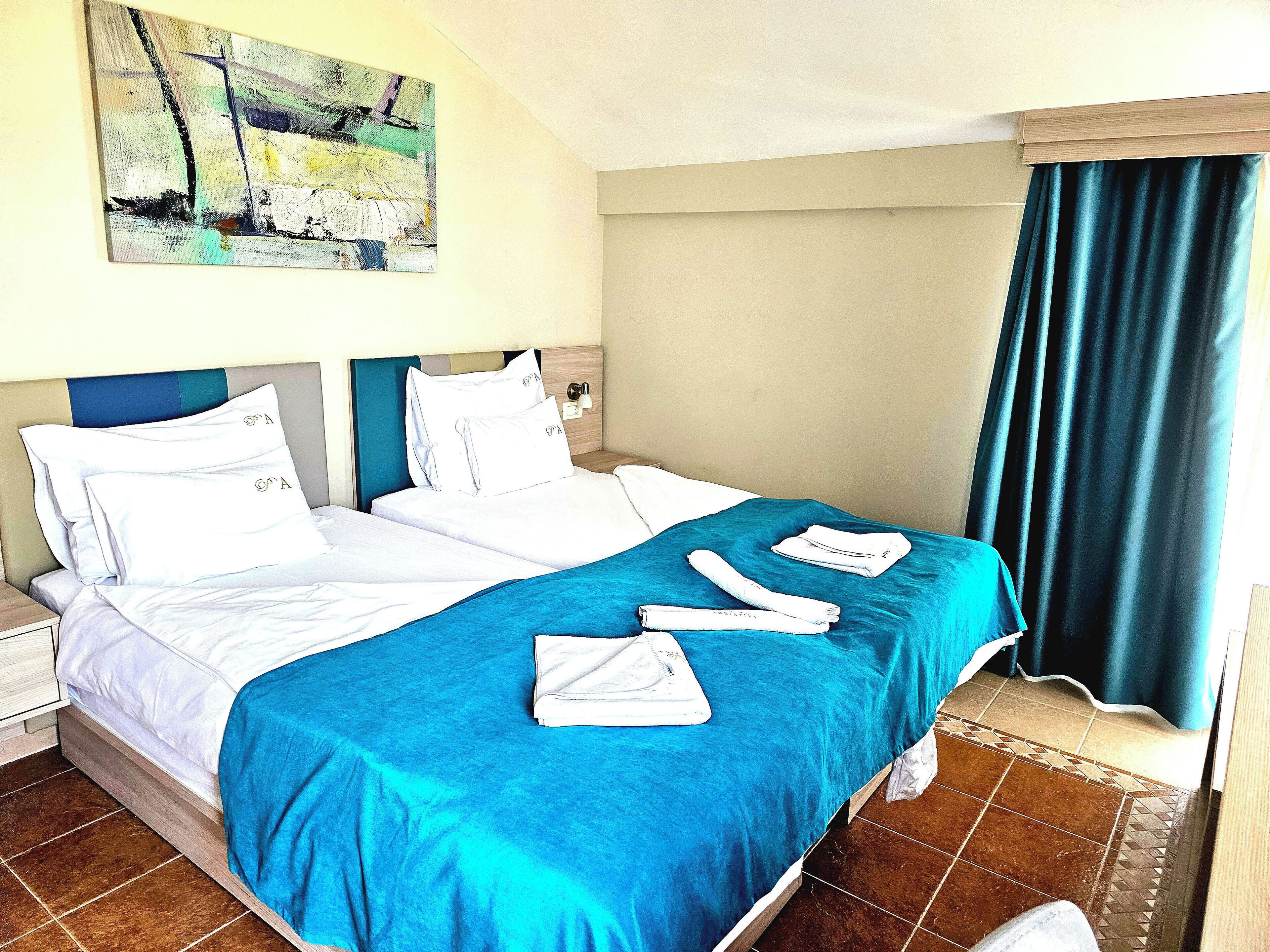Una habitación de hotel con una cama, un cuadro en la pared y una ventana con cortinas.