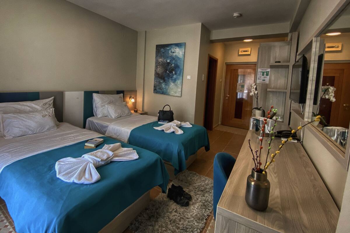 Une chambre d’hôtel avec deux lits, un bureau agrémenté d’un vase de fleurs et un tableau au mur.