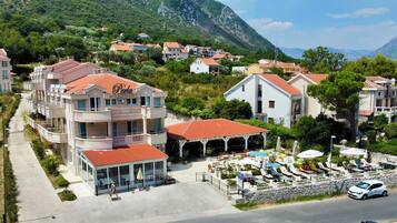 A coastal hotel with multiple balconies, a covered outdoor seating area, and a view of the surrounding hillside.