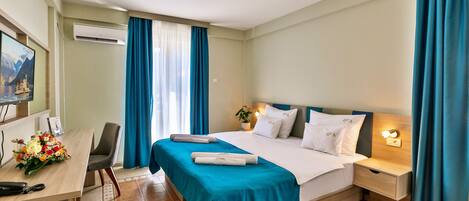 Habitación de hotel con cama, escritorio, silla, mesita de noche y aire acondicionado instalado en la pared.