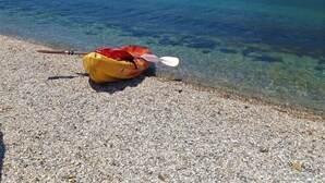 A kayak on a pebbled beach with clear water and mountains in the background.