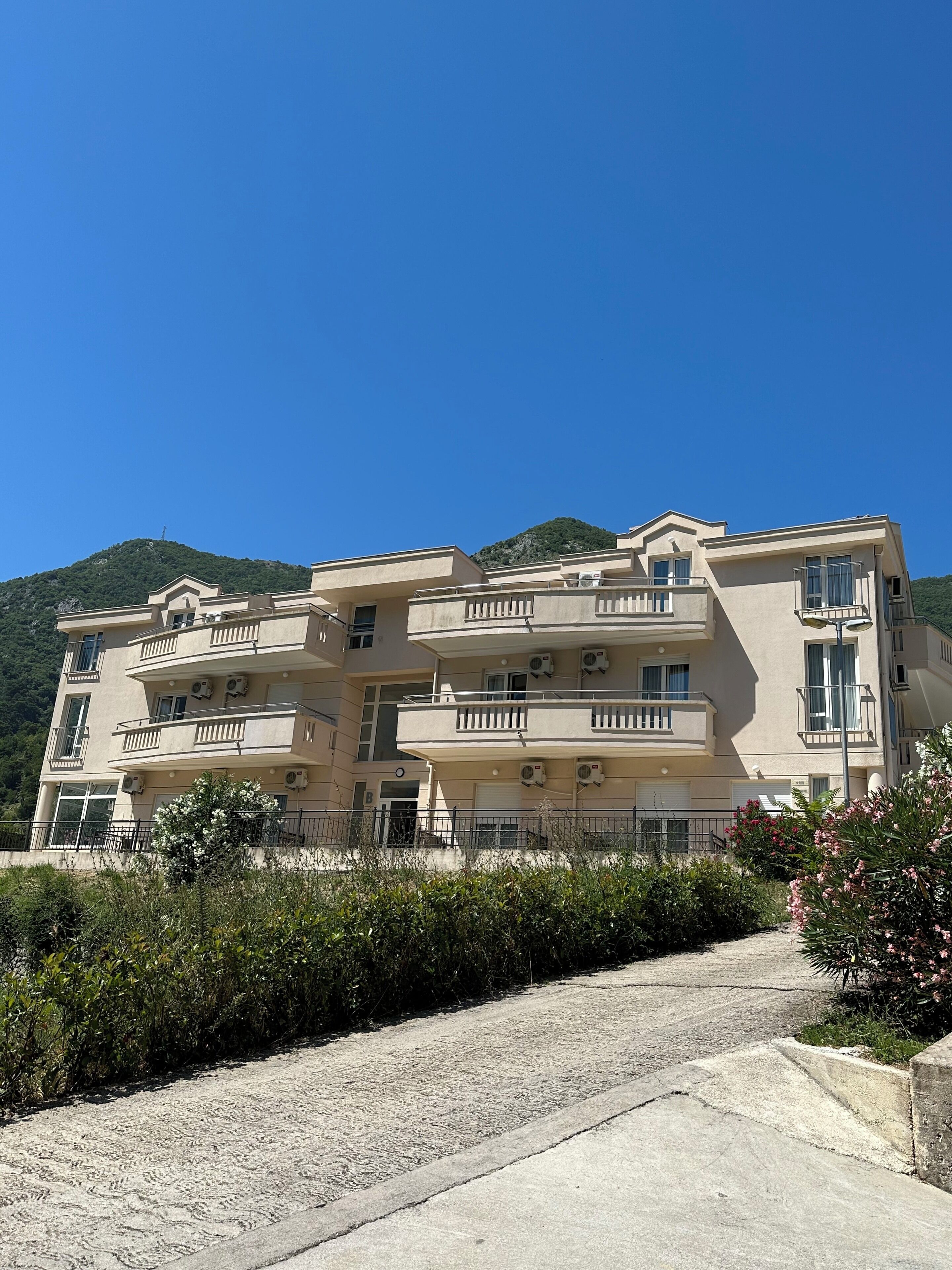 Un immeuble à plusieurs étages doté de balcons, de climatiseurs et d’une entrée pavée.