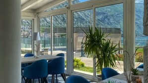 A sunlit room with a large table and blue chairs, large windows offering a view of the outdoors.