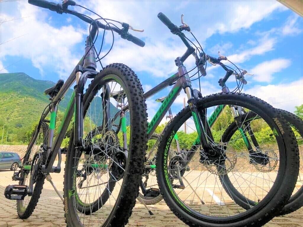 Dos bicicletas de montaña estacionadas sobre una superficie pavimentada, con un paisaje montañoso de fondo.