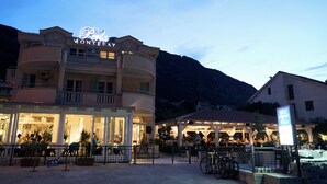 A hotel named "Perla Montebello" with outdoor seating and a mountain backdrop.