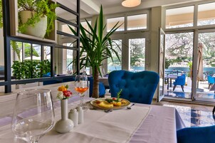 Un comedor con una mesa lista para dos personas, que incluye un plato de comida, un florero con flores y una copa de vino.