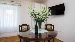Ein Essbereich mit einem runden Glastisch, zwei Holzstühlen, einer Blumenvase, einer Flasche und einem Glas.