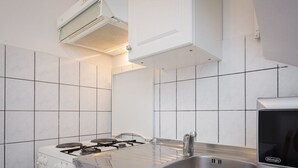 Eine moderne Küche mit weißen Fliesen, einem Gasherd, einer Edelstahl-Spüle und einem DeLonghi-Backofen.