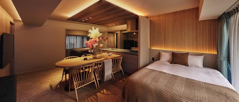 A hotel room with a bed, a desk with chairs, a vanity, and a television.