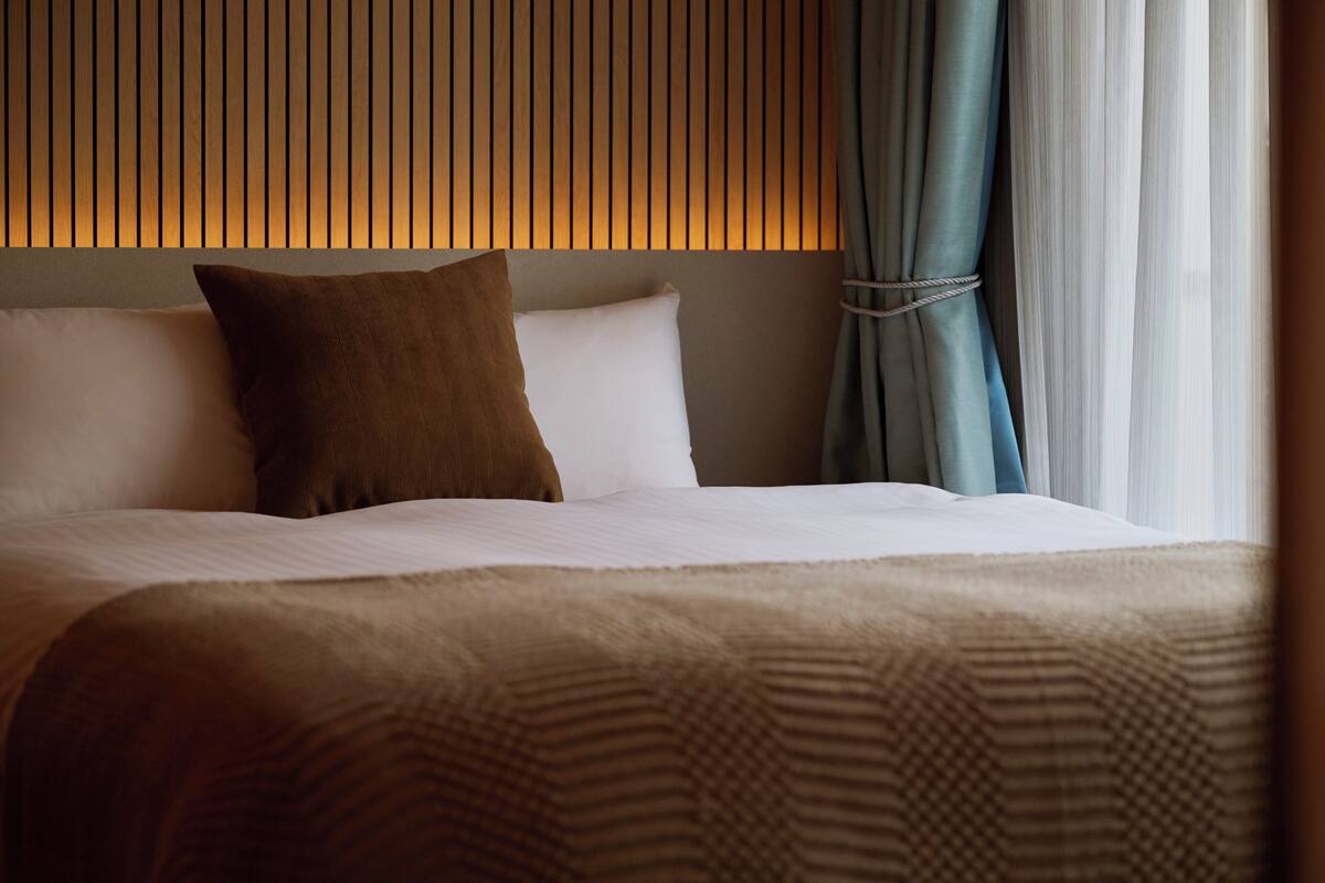 Un lit bien fait, avec une couverture à motifs, un oreiller marron et un oreiller blanc.