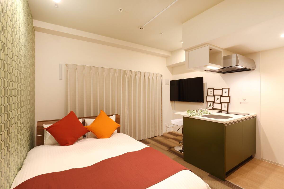 Une chambre d’hôtel avec un lit, une petite kitchenette, une télévision et une fenêtre avec des rideaux.