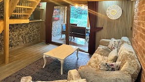 A cozy wooden interior with a stone wall, a sofa, a small table, and a staircase. - Nehir Bungalows (Camlihemsin)