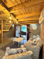 A cozy wooden interior with a stone wall, a sofa, a small table, and a staircase.