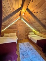 A cozy attic bedroom with two beds, wooden walls, and a sloped ceiling.