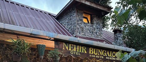 Un edificio de piedra con un letrero de neón que dice 'Nehir Bungalow' y un número de contacto.