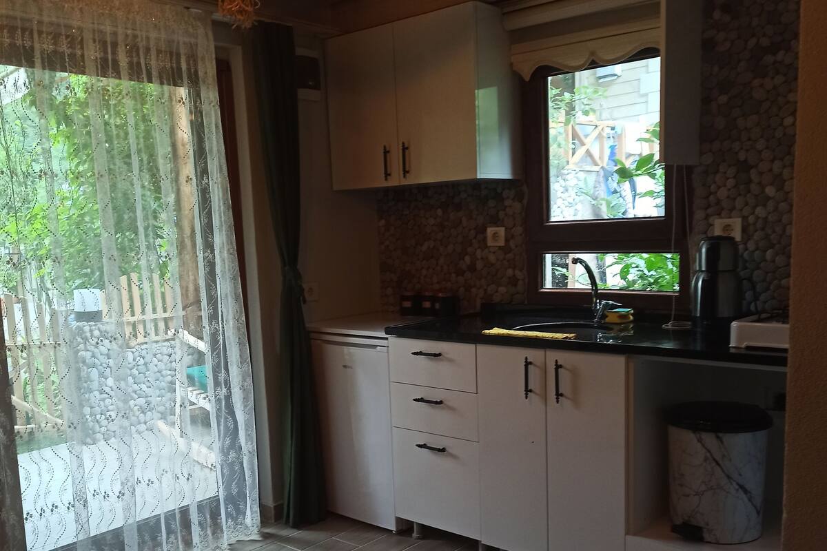Una cocina con armarios blancos, encimera negra y ventana con vistas a la vegetación.