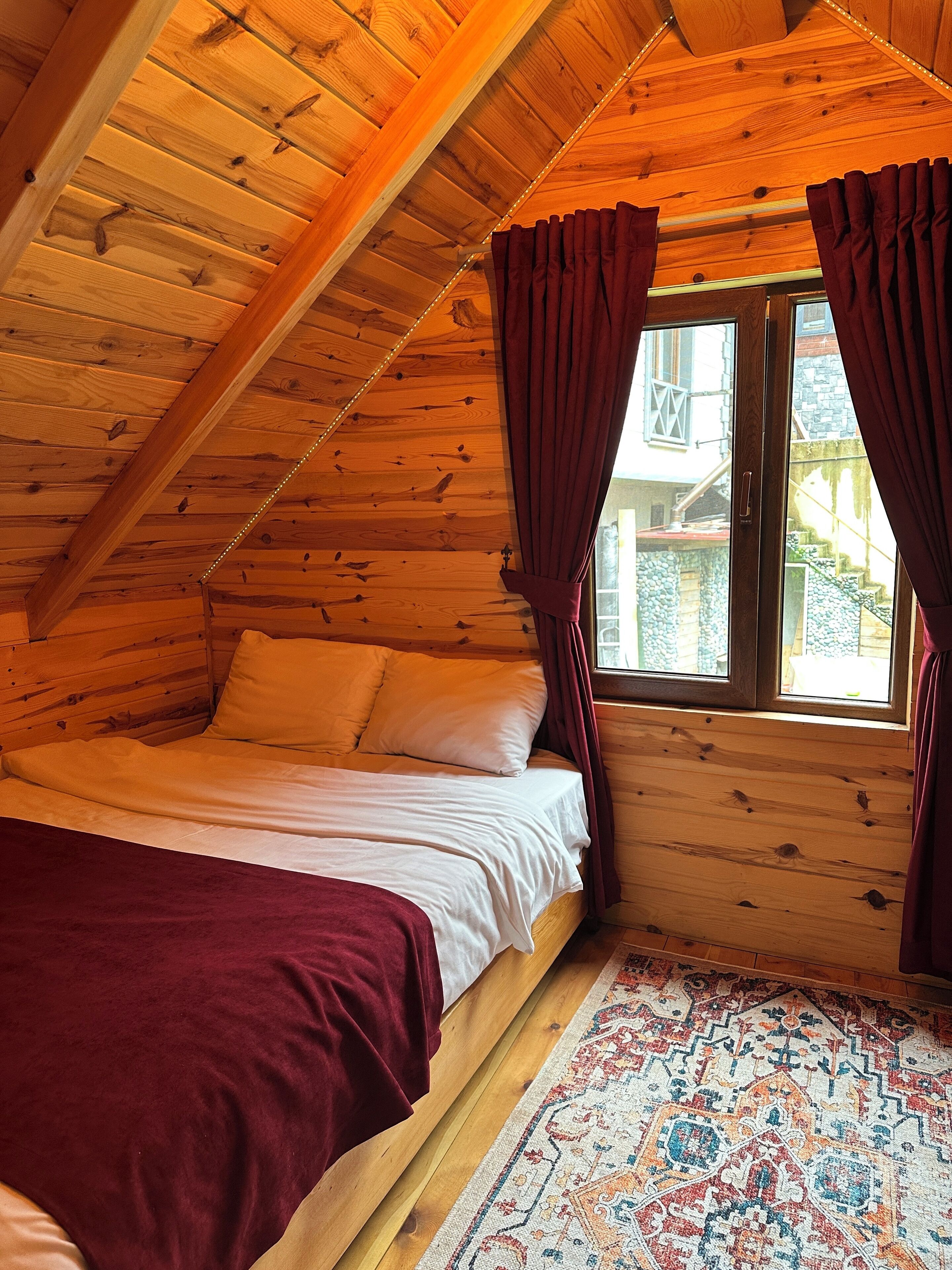 Acogedora habitación de cabaña de madera con cama, ventana con cortinas y una alfombra estampada.