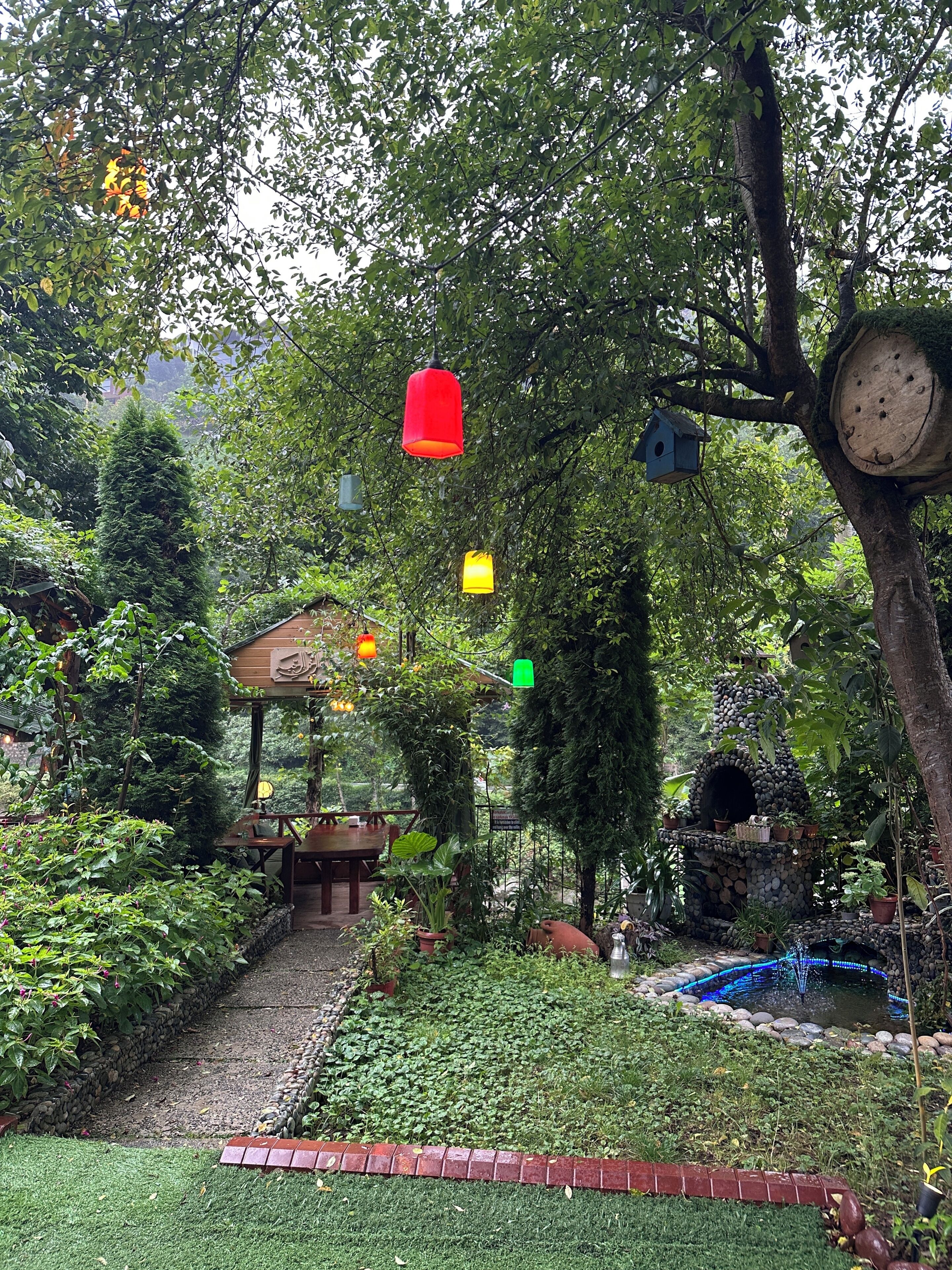 A garden with a wooden structure, a pond, and hanging birdhouses.