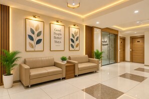 Vestíbulo de hotel con mostrador de recepción, dos sofás, obras de arte enmarcadas y una entrada con puerta de vidrio.