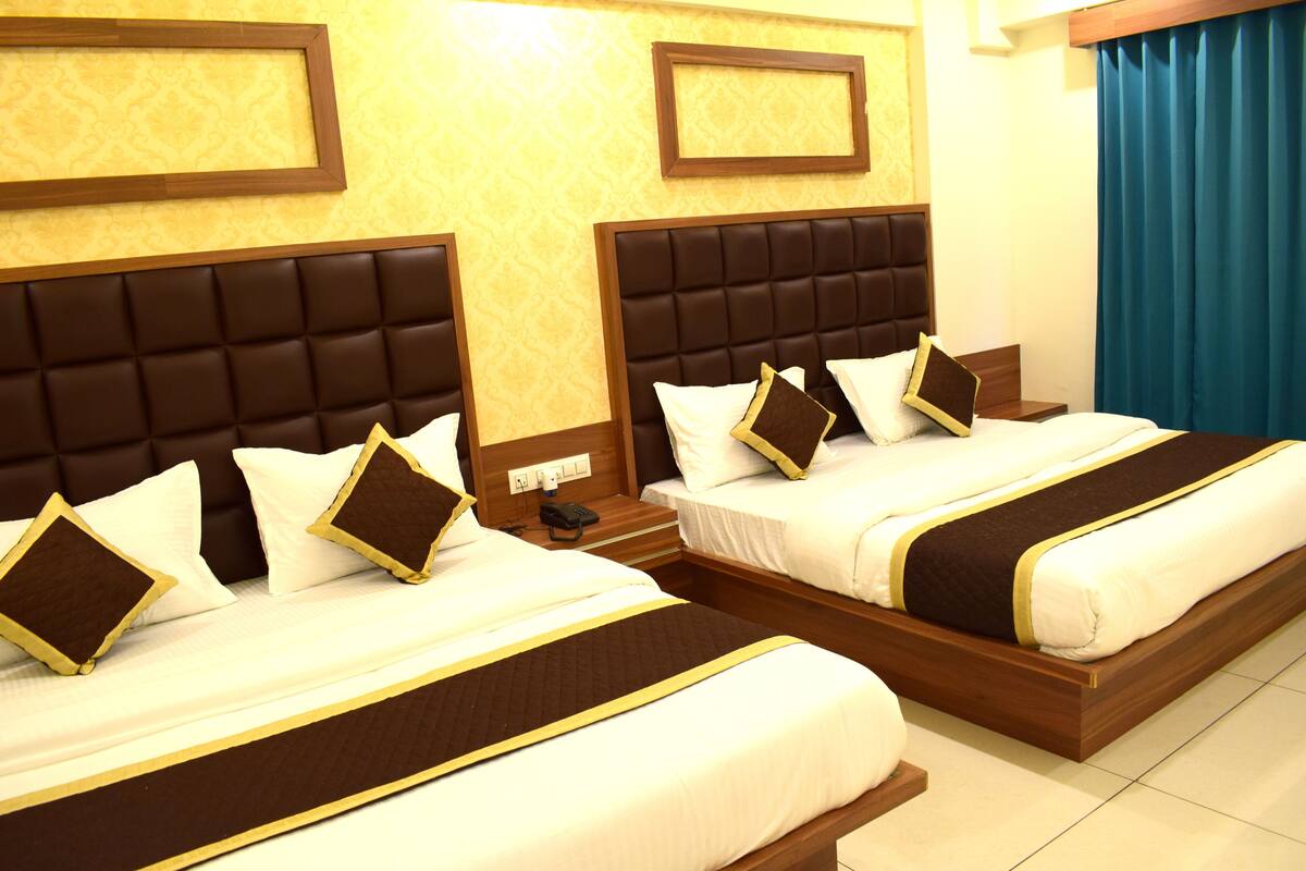 Habitación de hotel con dos camas, cada una con cabecera, ropa de cama blanca y detalles en tonos marrones.