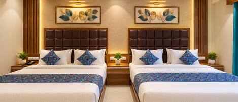 A hotel room with two beds, a central light fixture, and a decorative leaf wall art piece.