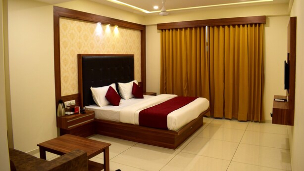 A modern hotel room with a large bed, wooden headboard, and a flat-screen TV. - Hotel Royal Square, Ahmedabad (Ahmedabad)