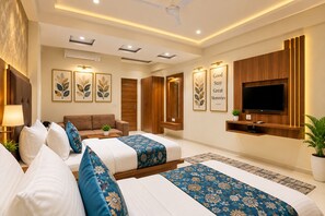 A modern hotel room with a sofa, two beds, a TV, and a wall-mounted TV.