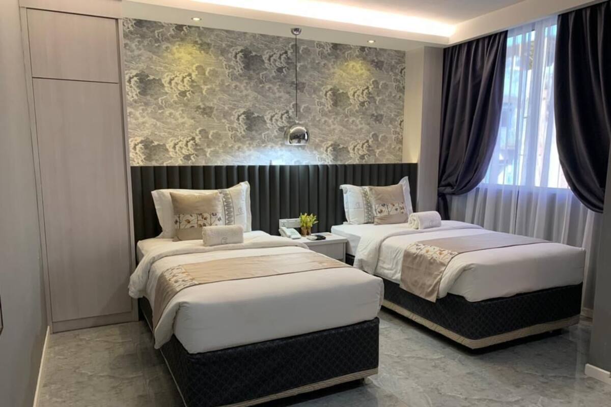 A modern hotel room with two beds, a marble floor, a textured wall, and a large window with curtains.