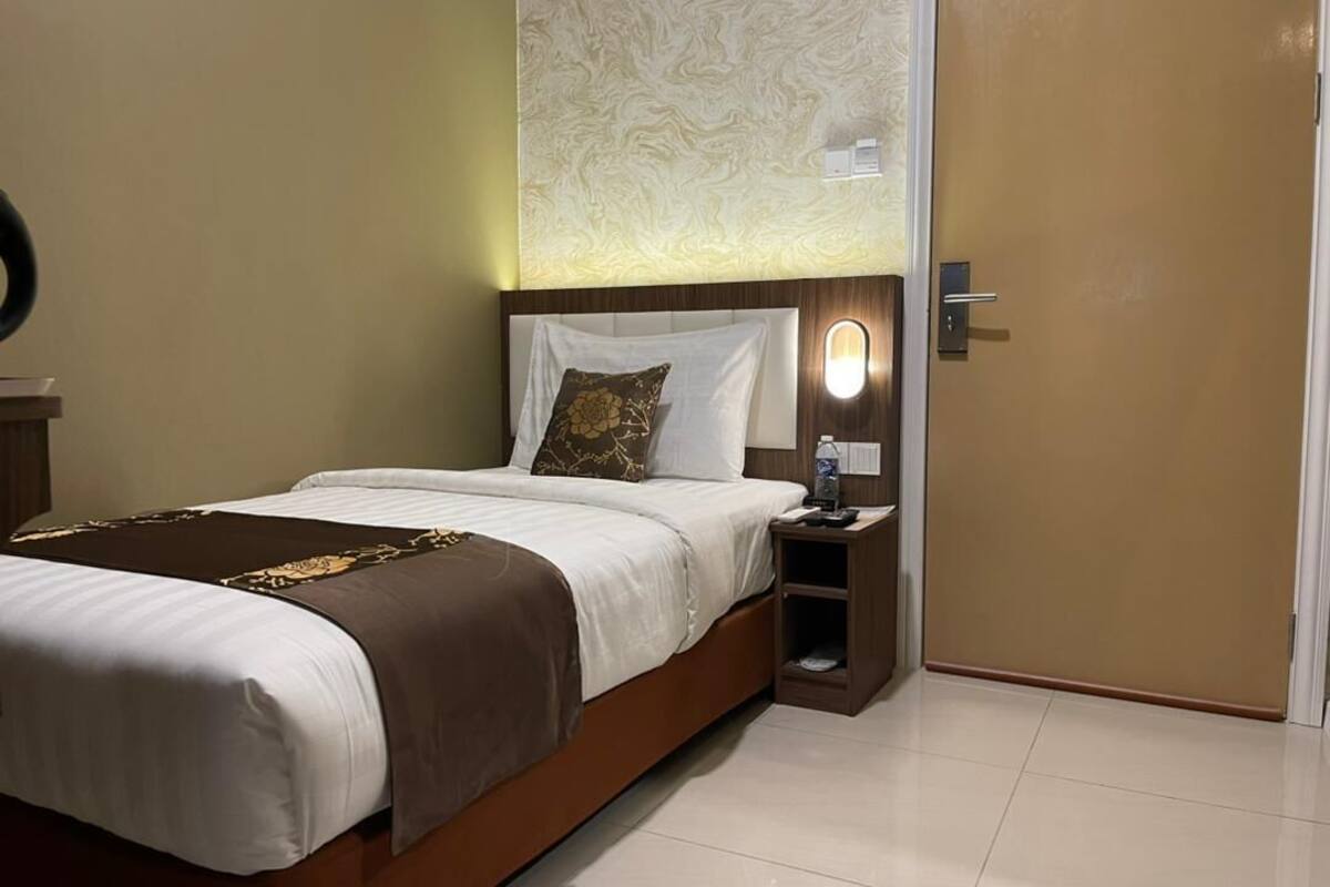 A neatly made bed with a brown and white bedspread, a bedside table with a lamp, and a wall with a textured pattern.