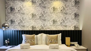 A hotel room with a large bed, a headboard with a cloud pattern, a bedside table with a lamp, and a nightstand with a phone. - Red City Hotel (Lawas)
