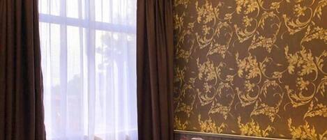 A hotel room with two beds, a large window with sheer curtains, and a patterned wallpaper.