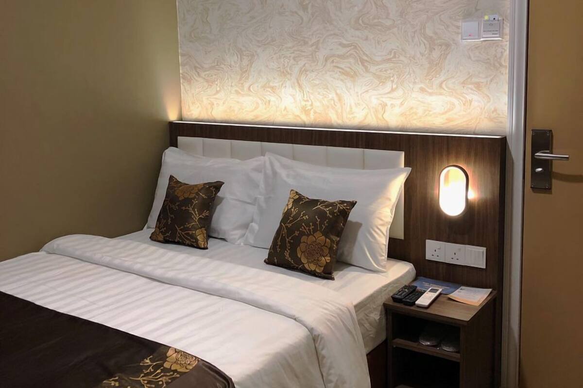 A hotel room with a large bed, a nightstand, and a wall-mounted light.