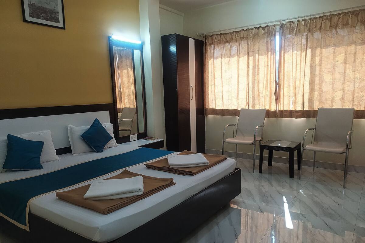 A hotel room with a bed, two chairs, a small table, and a mirror.