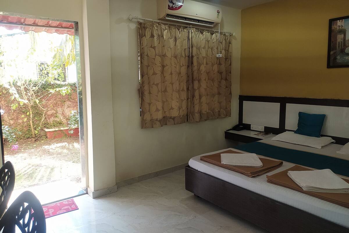 A bedroom with a bed, curtains, an air conditioning unit, and a view of the outdoors.