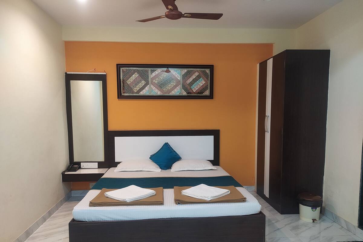A neatly made bed with a headboard, a bedside table, a mirror, and a framed artwork on the wall.