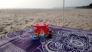 Escena de platja amb una manta, un recipient vermell i diversos objectes a sobre.