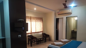 Habitació d'hotel amb llit, escriptori i cadira. Hi ha un aparell d'aire condicionat a la paret i un televisor també penjat a la paret.